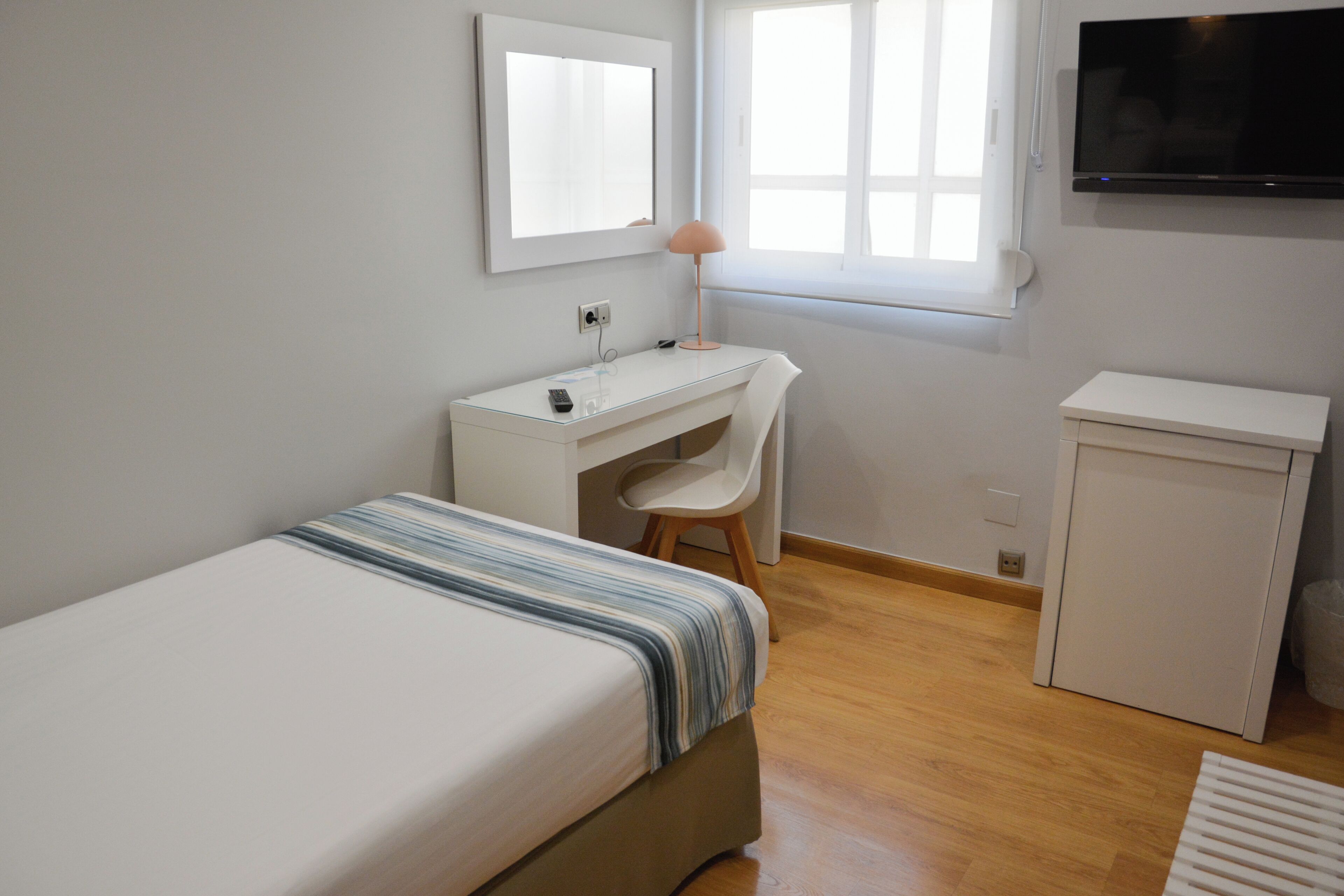 Un dormitorio con cama, escritorio, silla, televisor y un mueble pequeño.