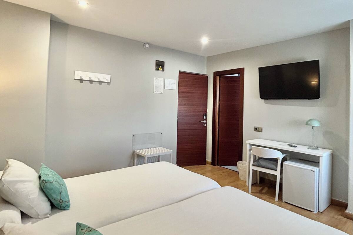 Una habitación de hotel con dos camas, un escritorio, un televisor y una puerta.
