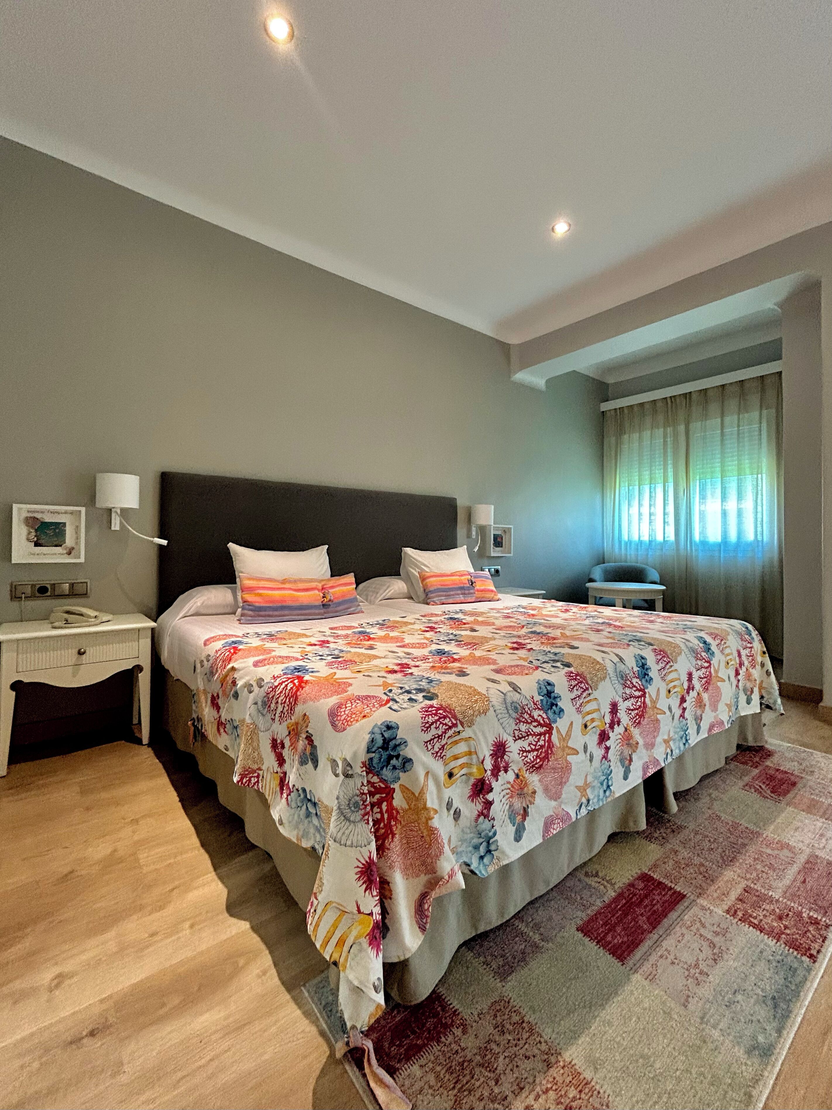 Un dormitorio con una cama grande, una mesita de noche, una lámpara y una ventana con cortinas.