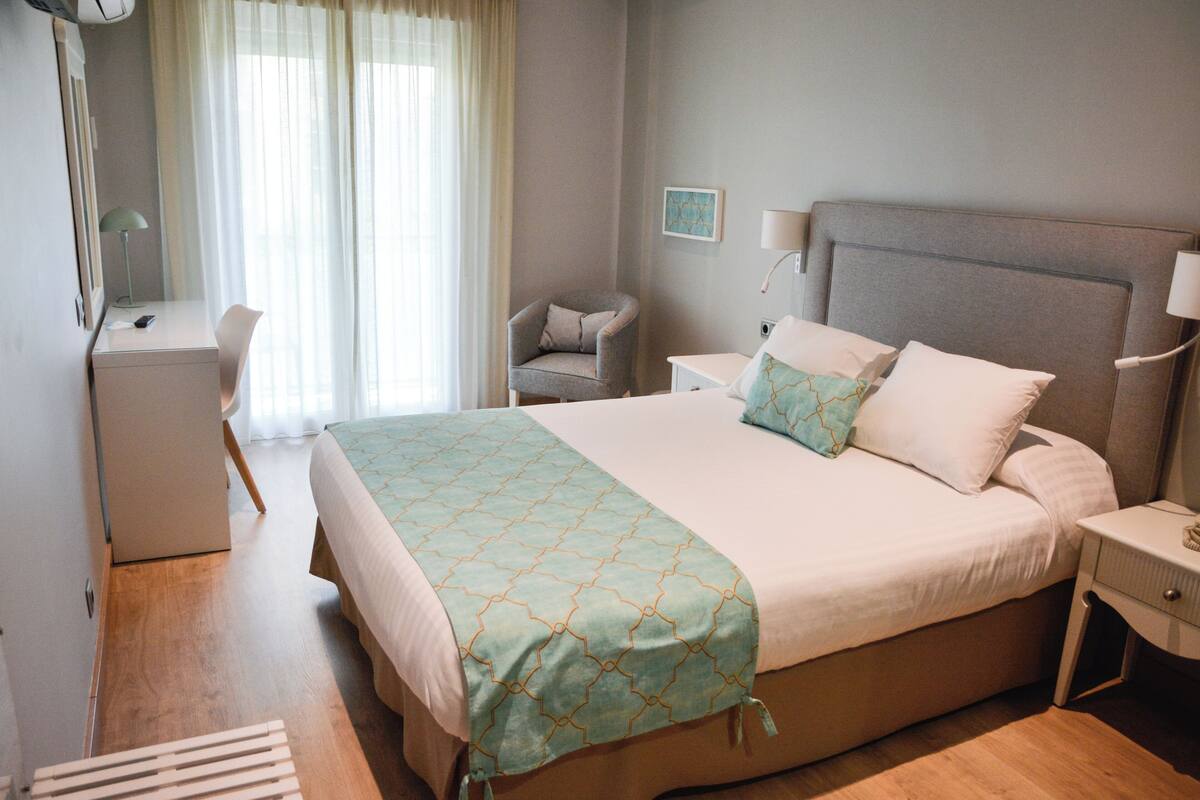 Una habitación de hotel con una cama grande, mesitas de noche, un escritorio y una silla.