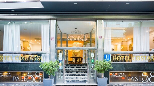 La entrada del Hotel CostaSol con fachada de vidrio, una escalera que conduce al vestíbulo y plantas en macetas a ambos lados.