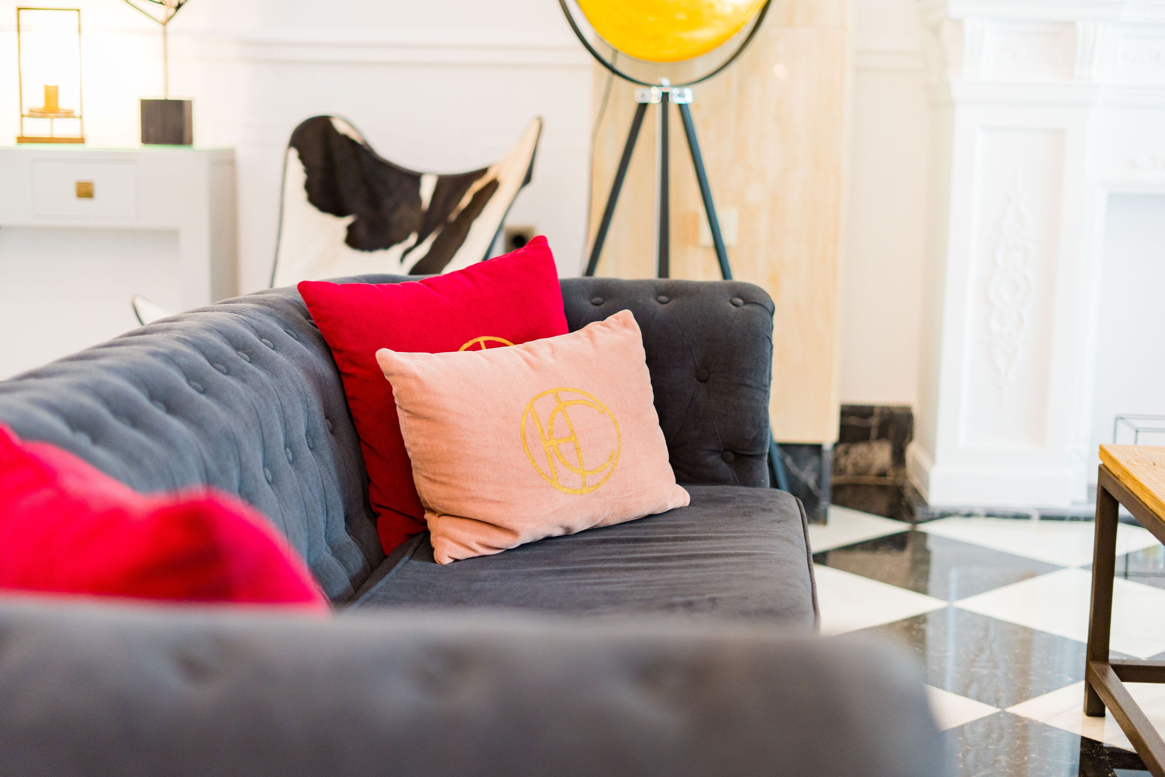 A modern living room with a grey sofa, red and pink cushions, a floor lamp, and a checkered floor.