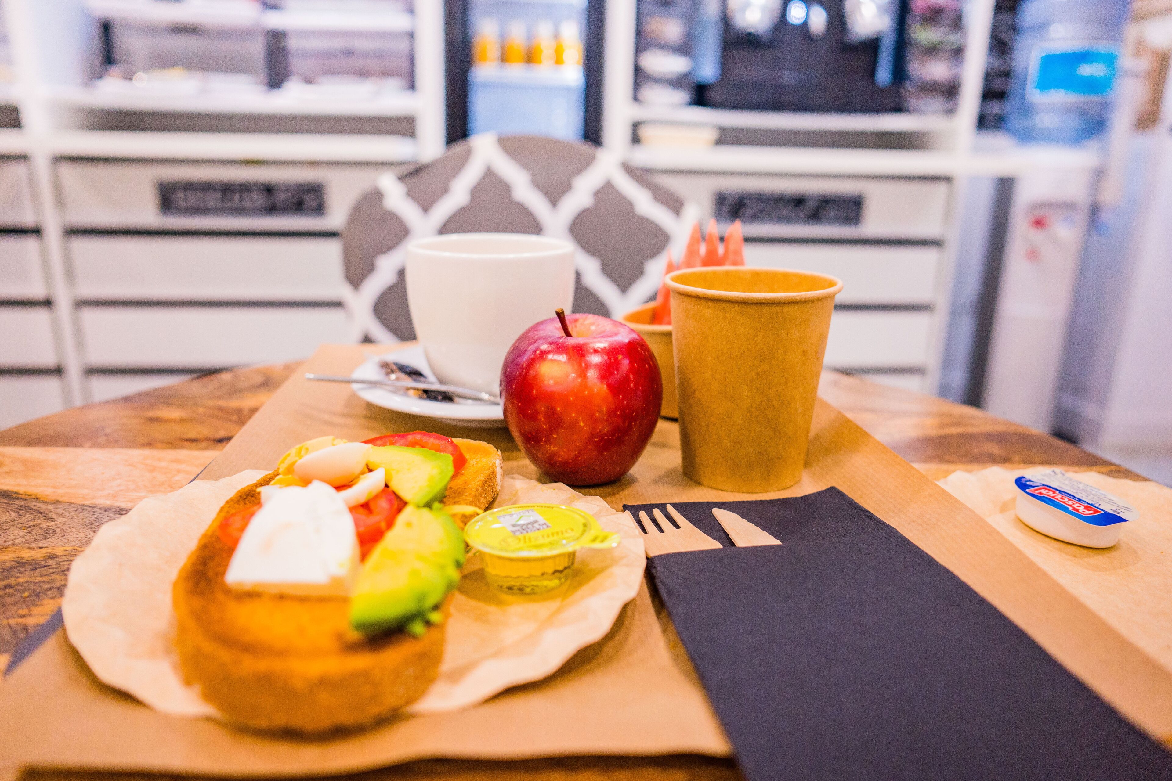 A meal with a sandwich, apple, cup, and condiments on a table.