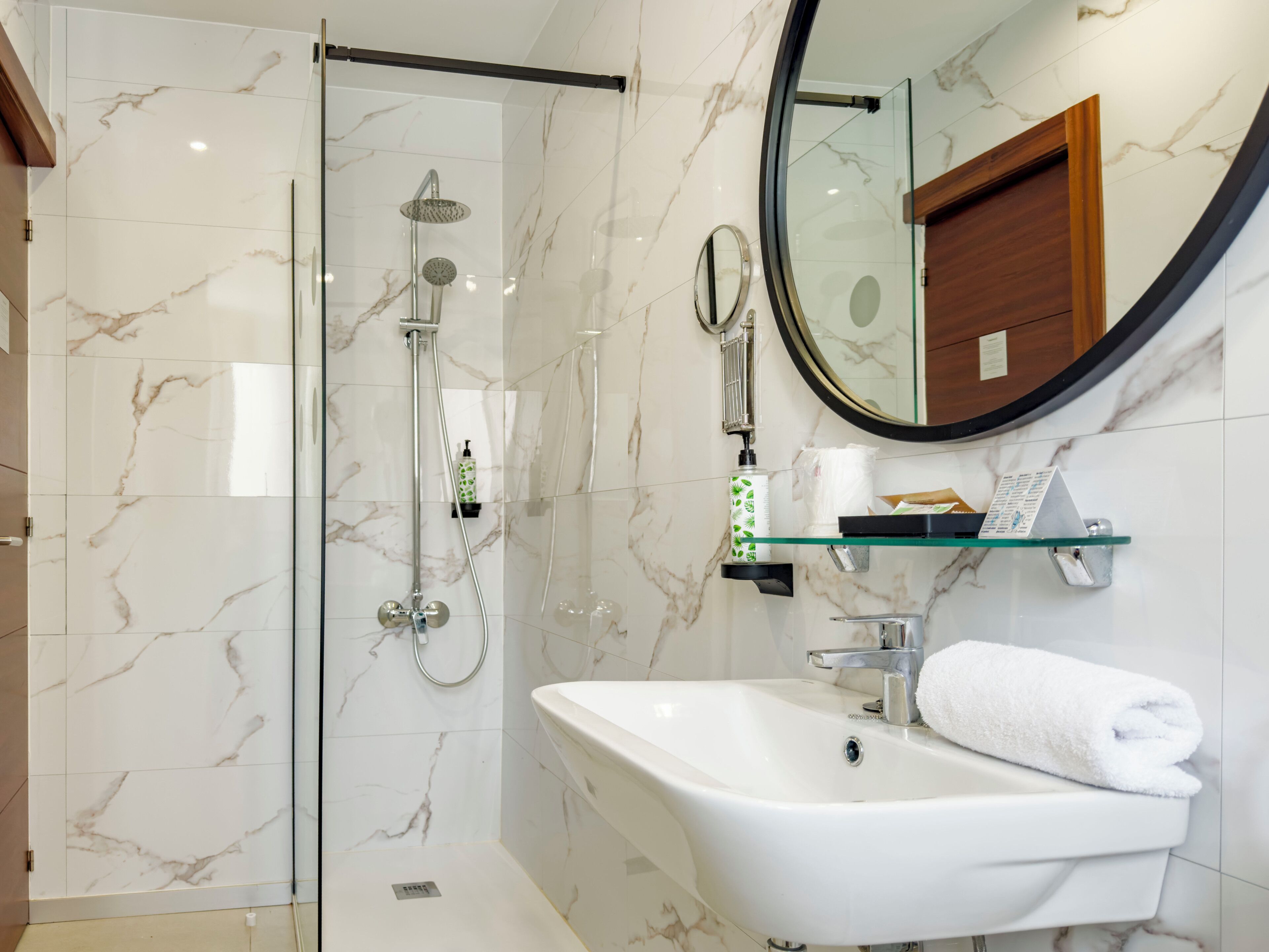 Un baño moderno con ducha de vidrio, lavamanos blanco y espejo redondo.