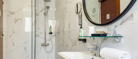 Un baño moderno con ducha de vidrio, lavamanos blanco y espejo redondo.