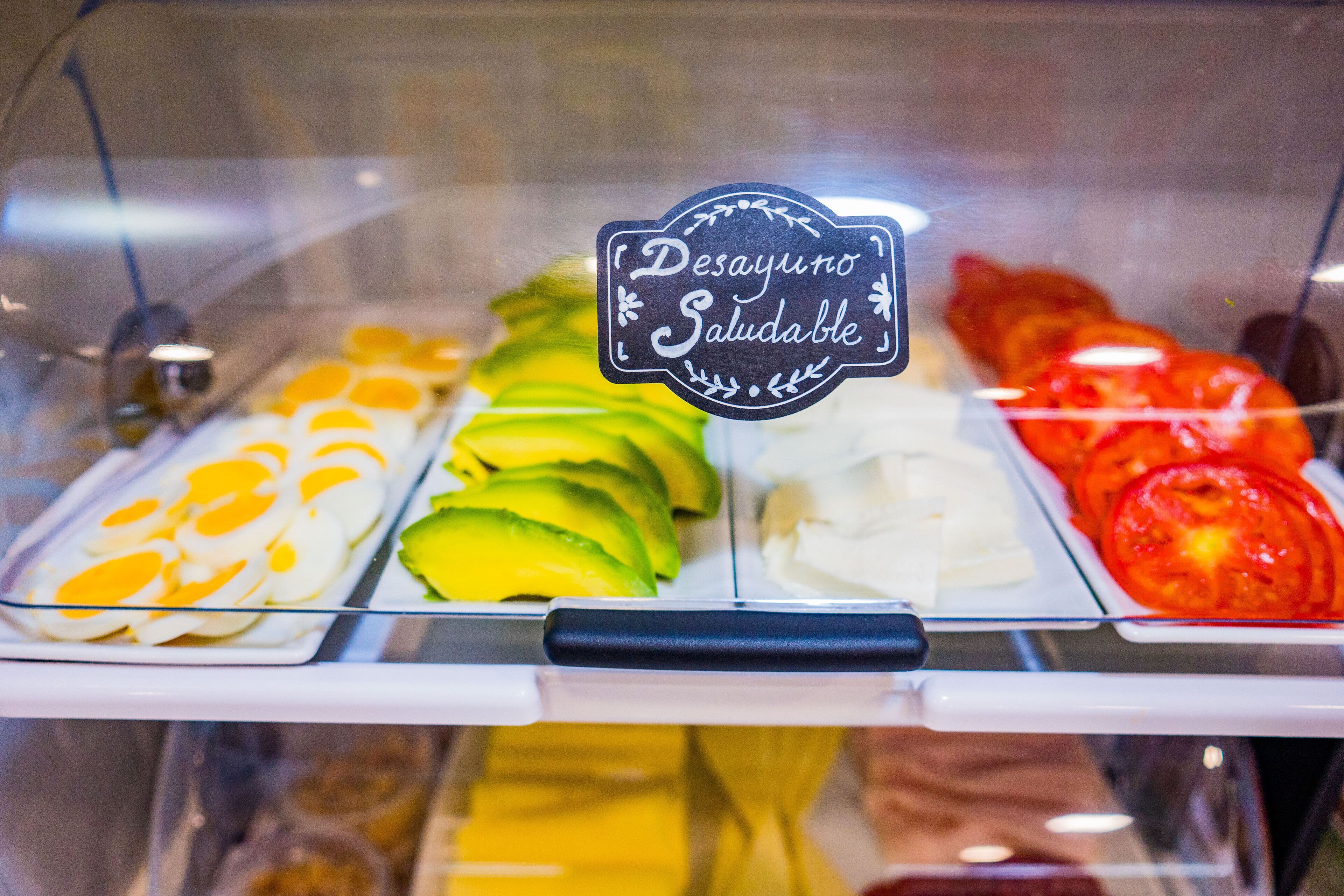 A food display case with sliced eggs, avocado, cheese, and tomatoes.