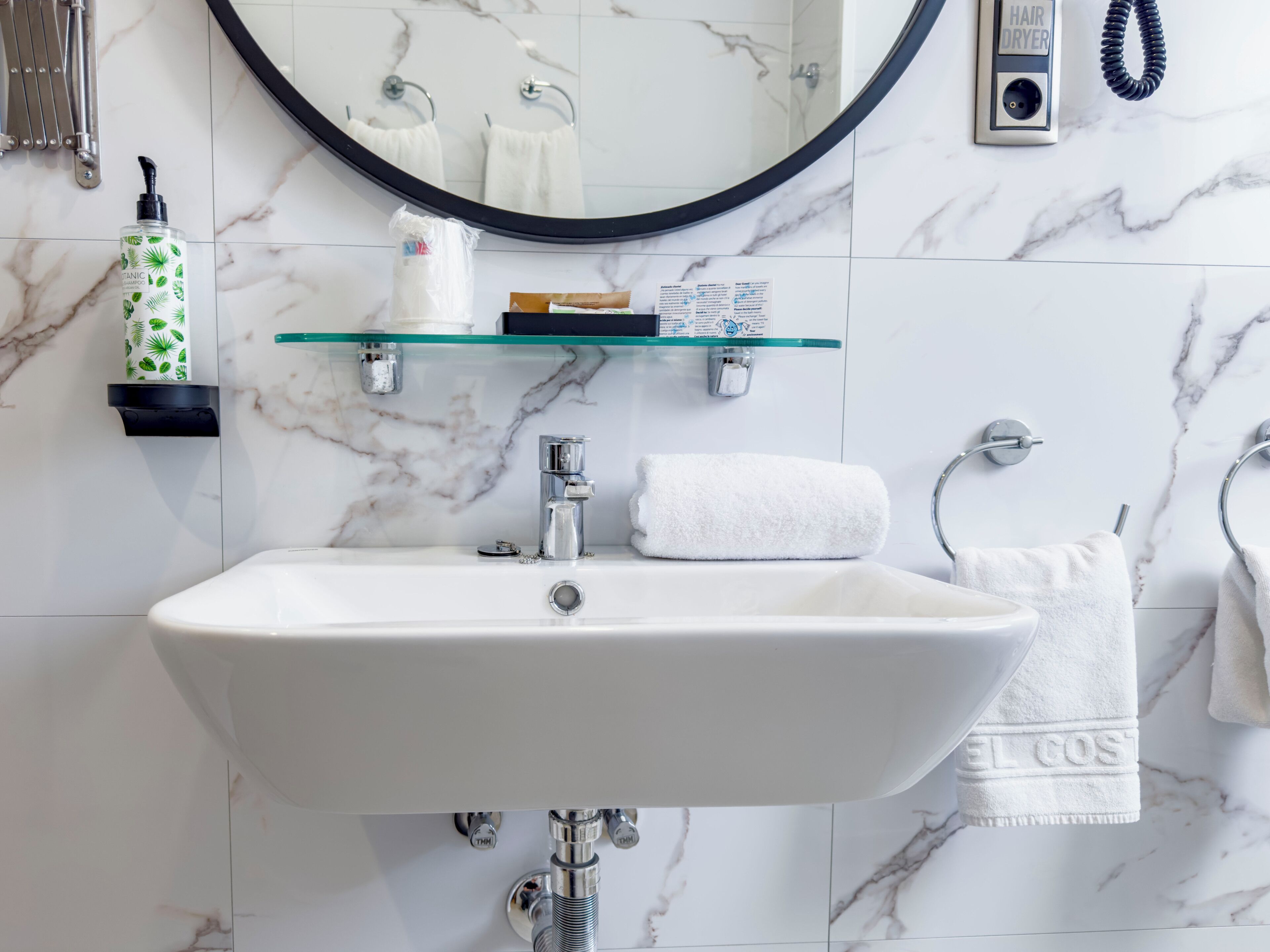 Une salle de bain avec un lavabo blanc, un miroir rond et un porte-serviettes.