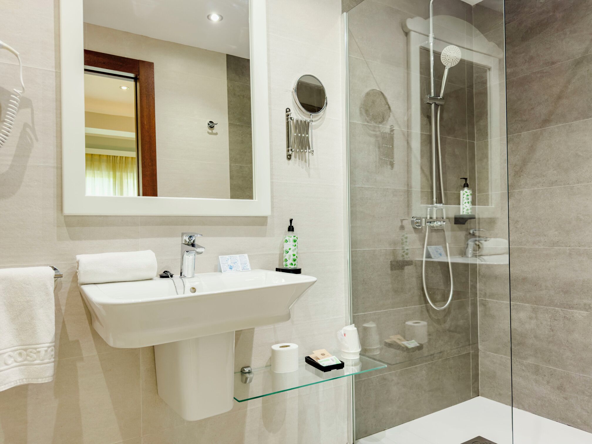Un baño moderno con cabina de ducha de vidrio, un lavabo blanco y un espejo encima.