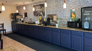 Zona de recepción de hotel con mostrador, máquinas de café, y una pizarra con el mensaje 'Buenos días', además de un microondas.