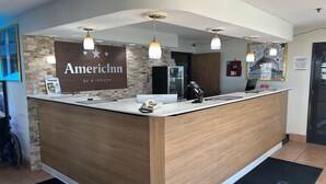 Una zona de recepción con mostrador de madera, un cartel que dice 'AmericInn by Wyndham' y un refrigerador.