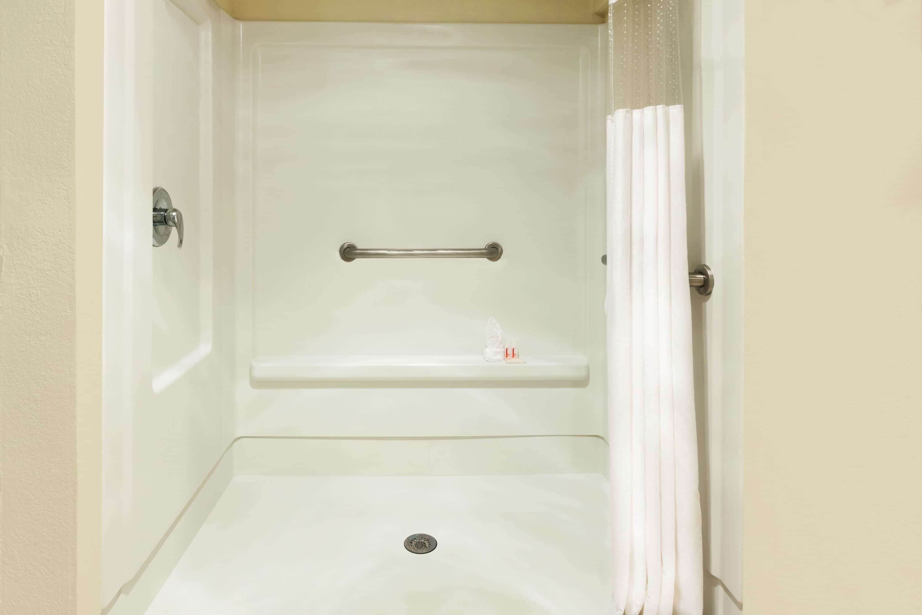 Un baño con ducha, barras de apoyo y un estante con artículos de aseo.