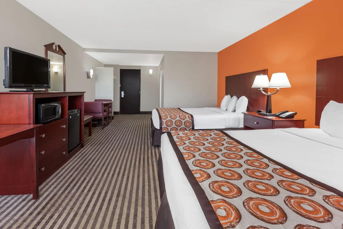 Een hotelkamer met een bed, een bureau met een televisie, een lamp en een deur naar een andere kamer.