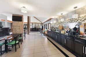 A modern kitchen with black cabinets, a long countertop, and a dining area with green chairs.