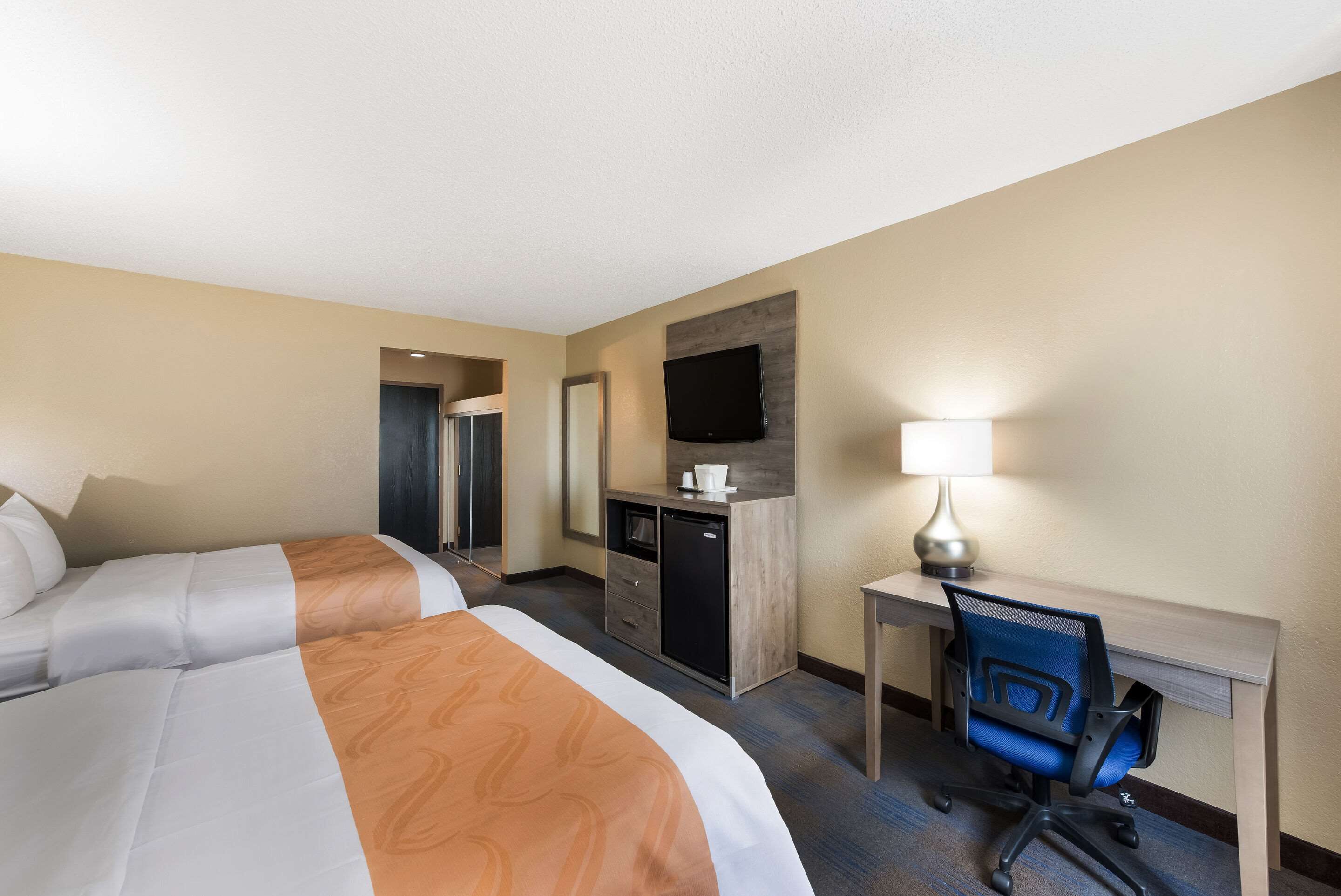 A hotel room with two beds, a desk, a chair, a TV, and a desk lamp.