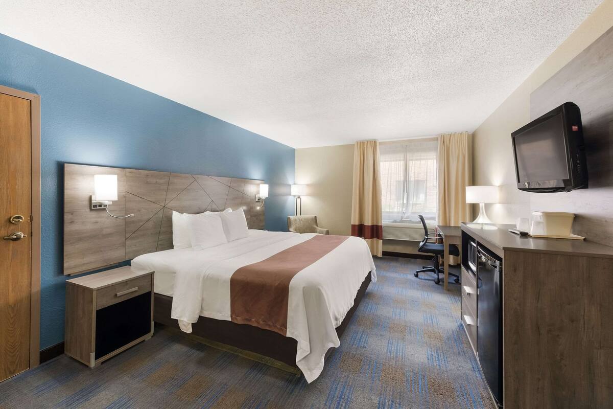 Una habitación de hotel con una cama grande, mesitas de noche, un escritorio con silla, televisión y una ventana con cortinas.