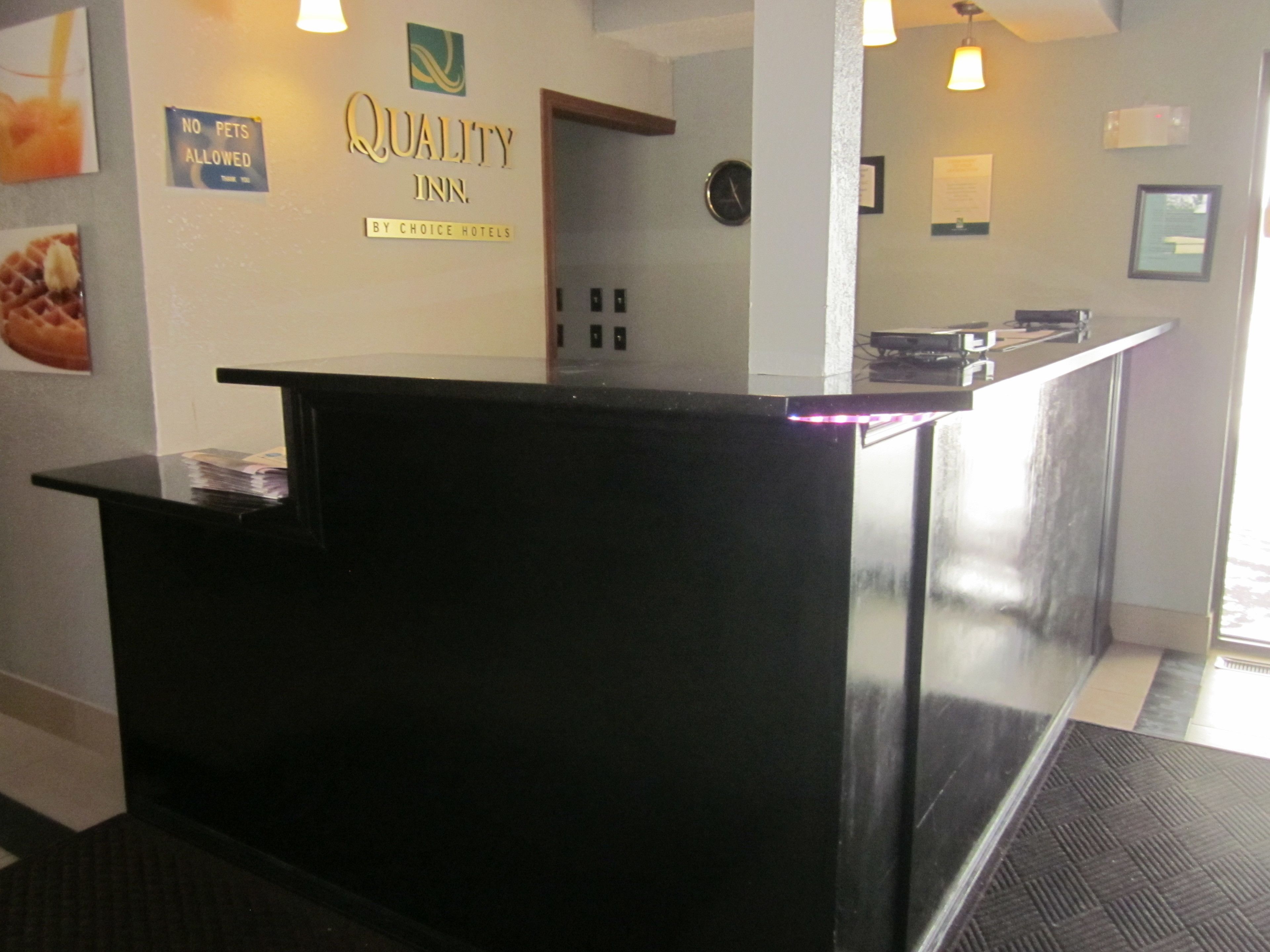 A hotel reception desk with a sign reading "Quality Inn" and "No Pets Allowed".
