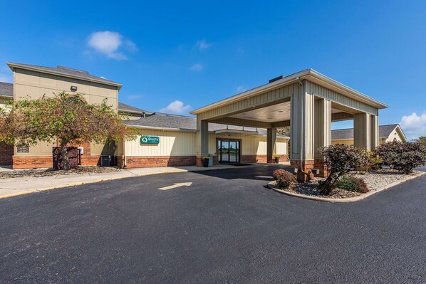 A hotel entrance with a covered waiting area, a clear sky, and a sign indicating 'Quality'.