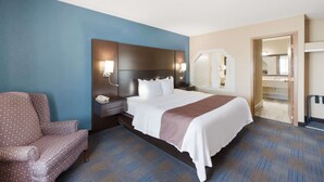 Habitación de hotel con una cama grande, una mesita de noche, una silla y un baño visible a través de una puerta abierta.
