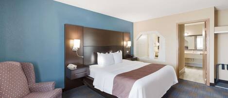 Habitación de hotel con una cama grande, una mesita de noche, una silla y un baño visible a través de una puerta abierta.