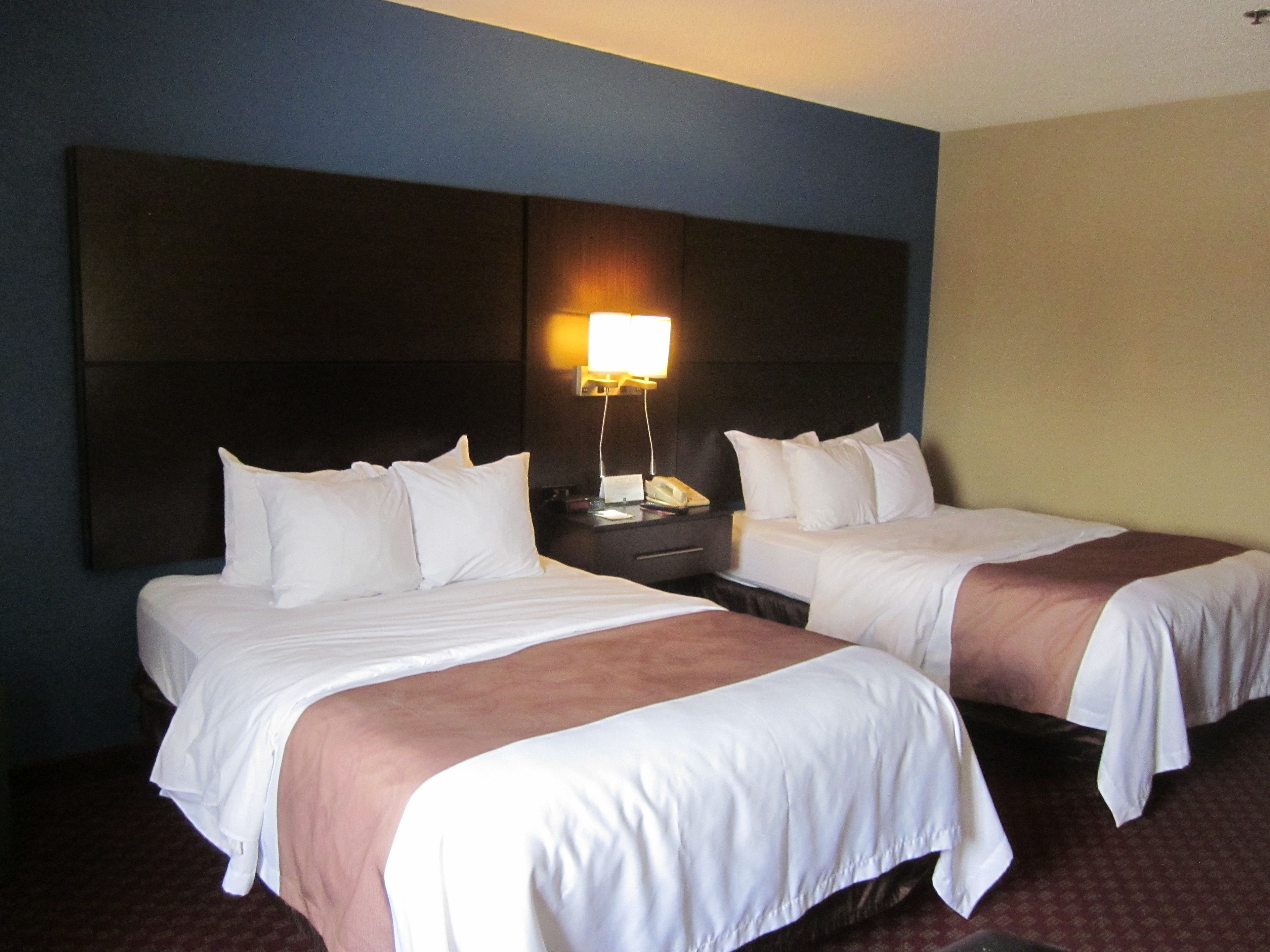 A hotel room with two beds, a nightstand with a lamp, and a telephone.