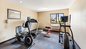 Un gimnasio con cintas de correr, elíptica y bicicleta estática. Se ve un coche y árboles a través de la ventana.