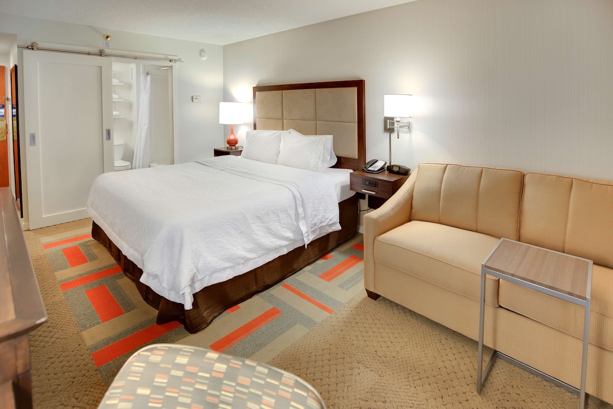Una habitación de hotel con cama, sofá, mesita de noche, lámpara y teléfono.