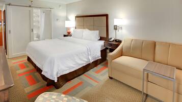 A hotel room with a bed, a sofa, a nightstand, a lamp, and a telephone.