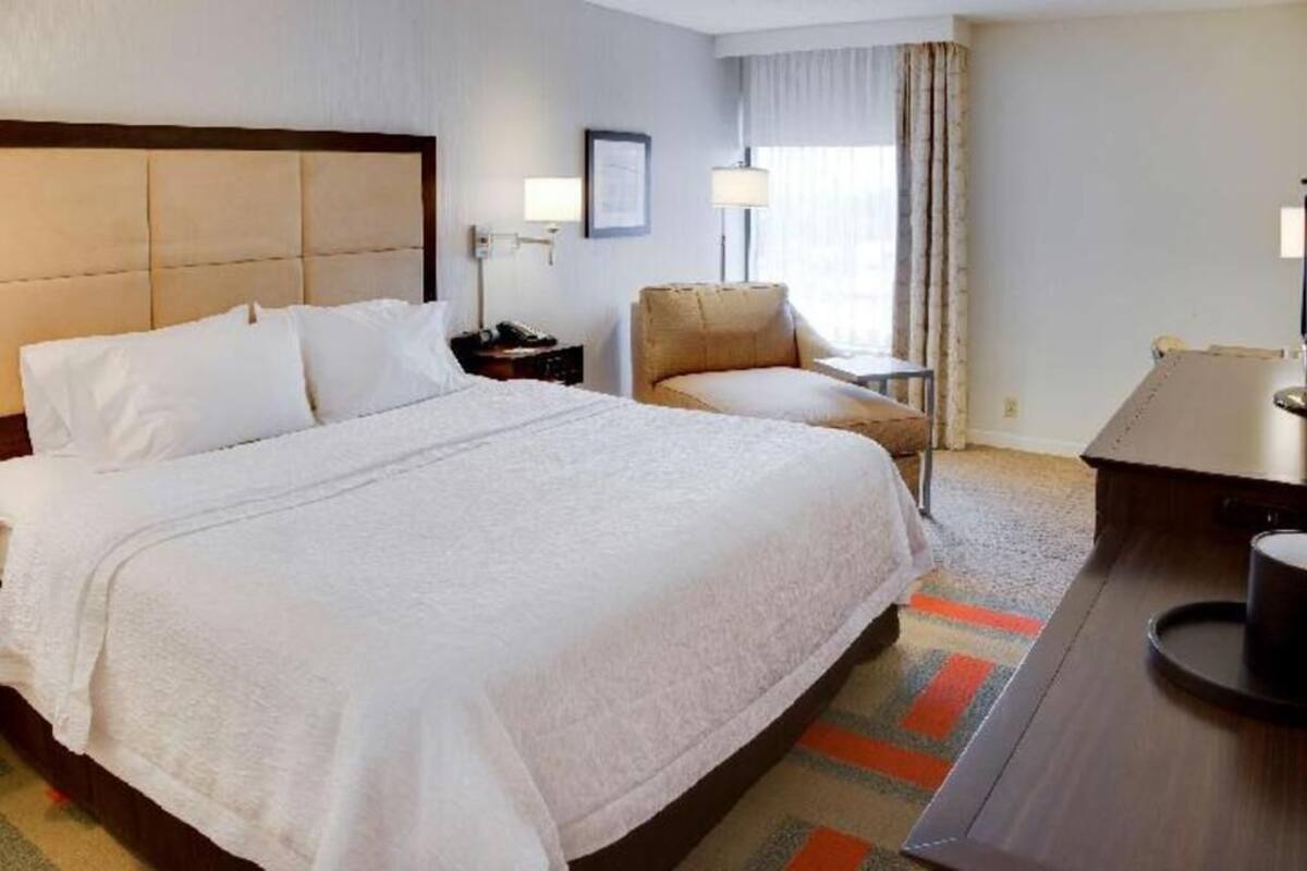 Una habitación de hotel con una cama grande, una silla, un escritorio y una lámpara.