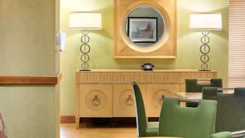 Habitación de hotel con un armario de madera, dos sillas verdes, una mesa redonda y un espejo en la pared.