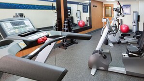 Ein Fitnessstudio mit Cardiogeräten, Gewichten und einem digitalen Bildschirm.