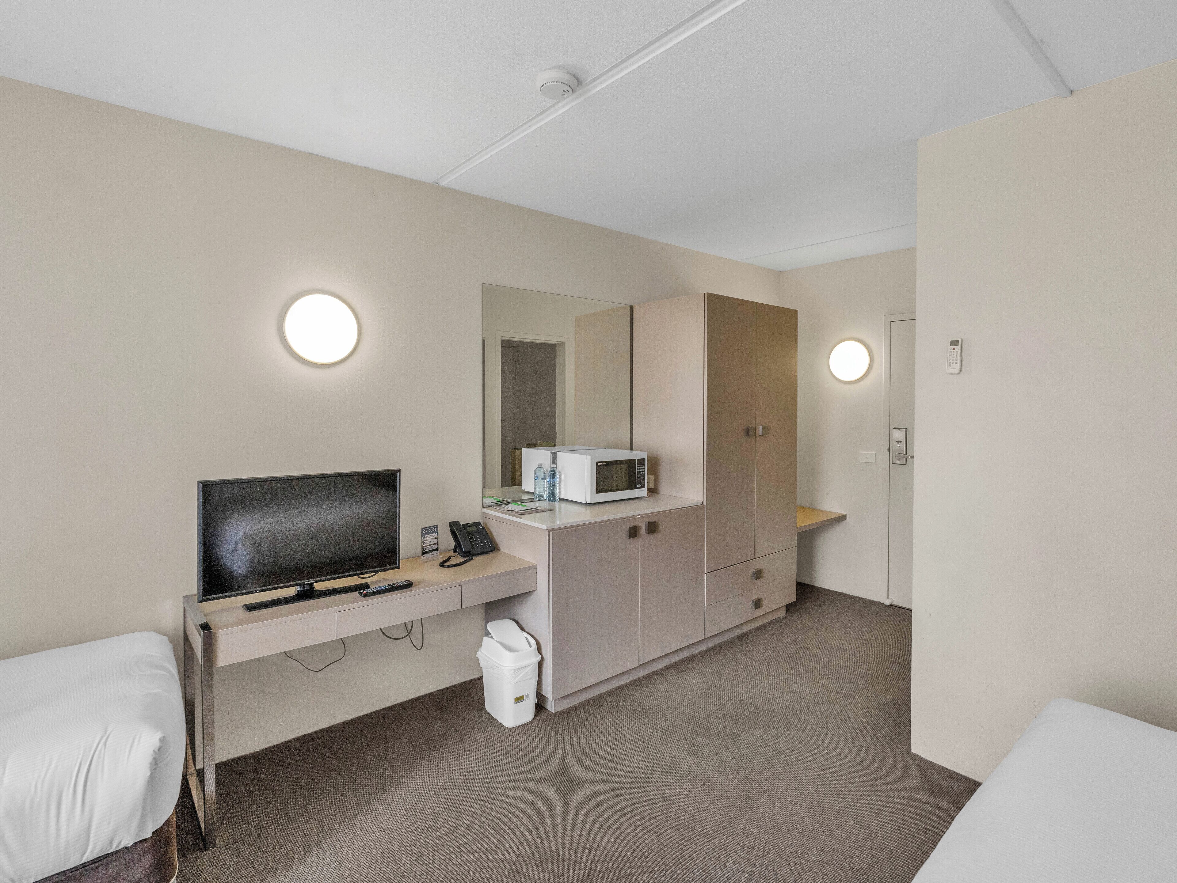 A hotel room with a bed, a desk with a TV, a microwave, a trash bin, and a wardrobe.