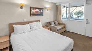 A hotel room with a large bed, a chair, a desk, and a window with curtains. - Tall Trees Ainslie Motel (Ainslie)