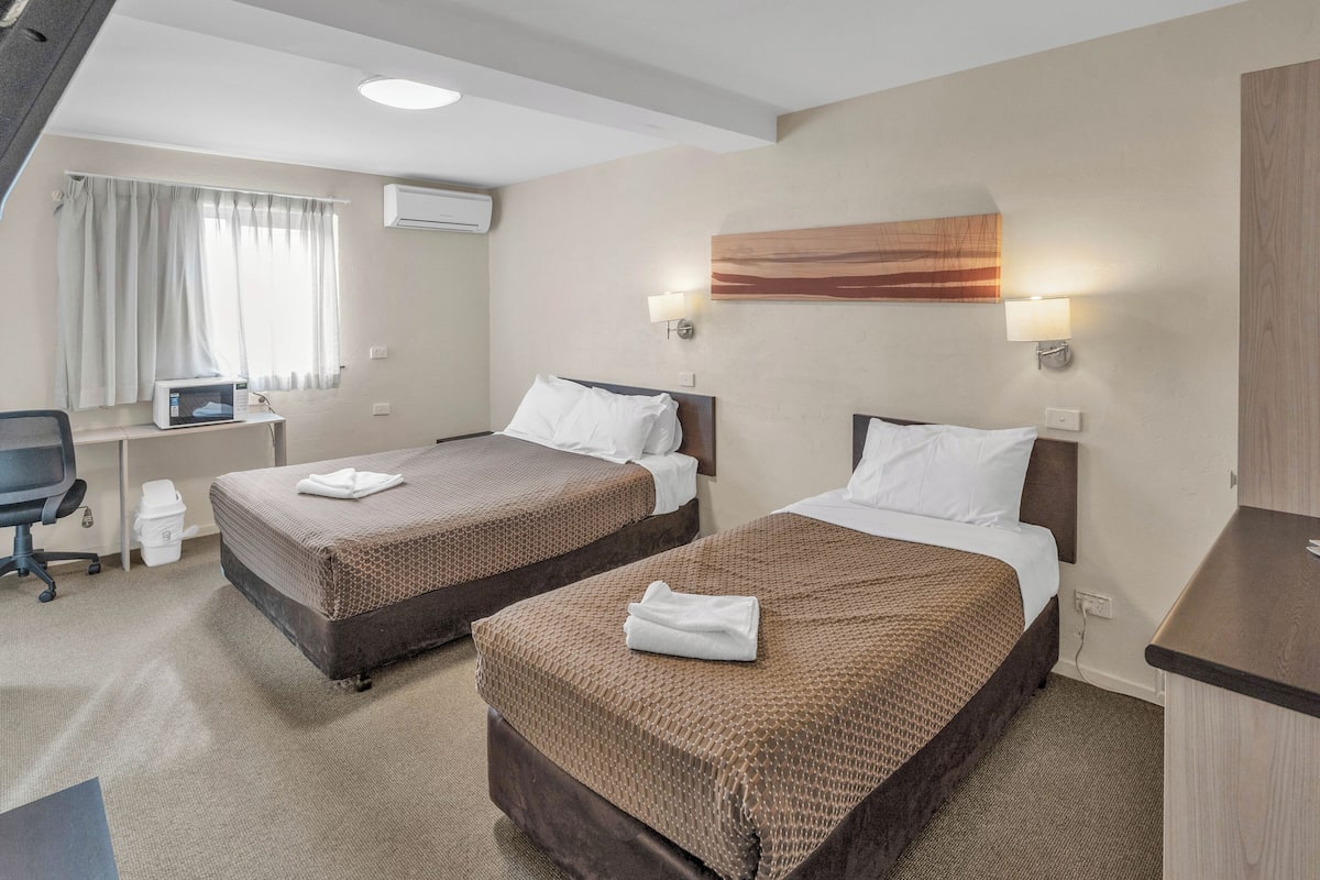 A hotel room with two beds, a desk, a chair, a microwave, and a window with curtains.