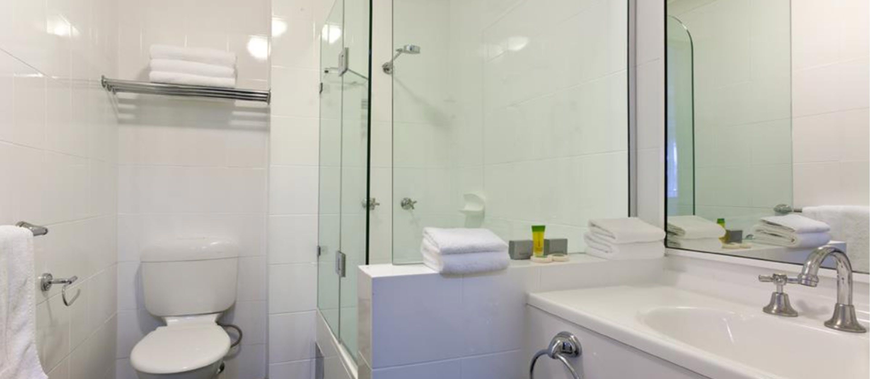 Une salle de bain moderne avec une douche à parois de verre, des toilettes blanches, un lavabo avec un miroir et un porte-serviettes.