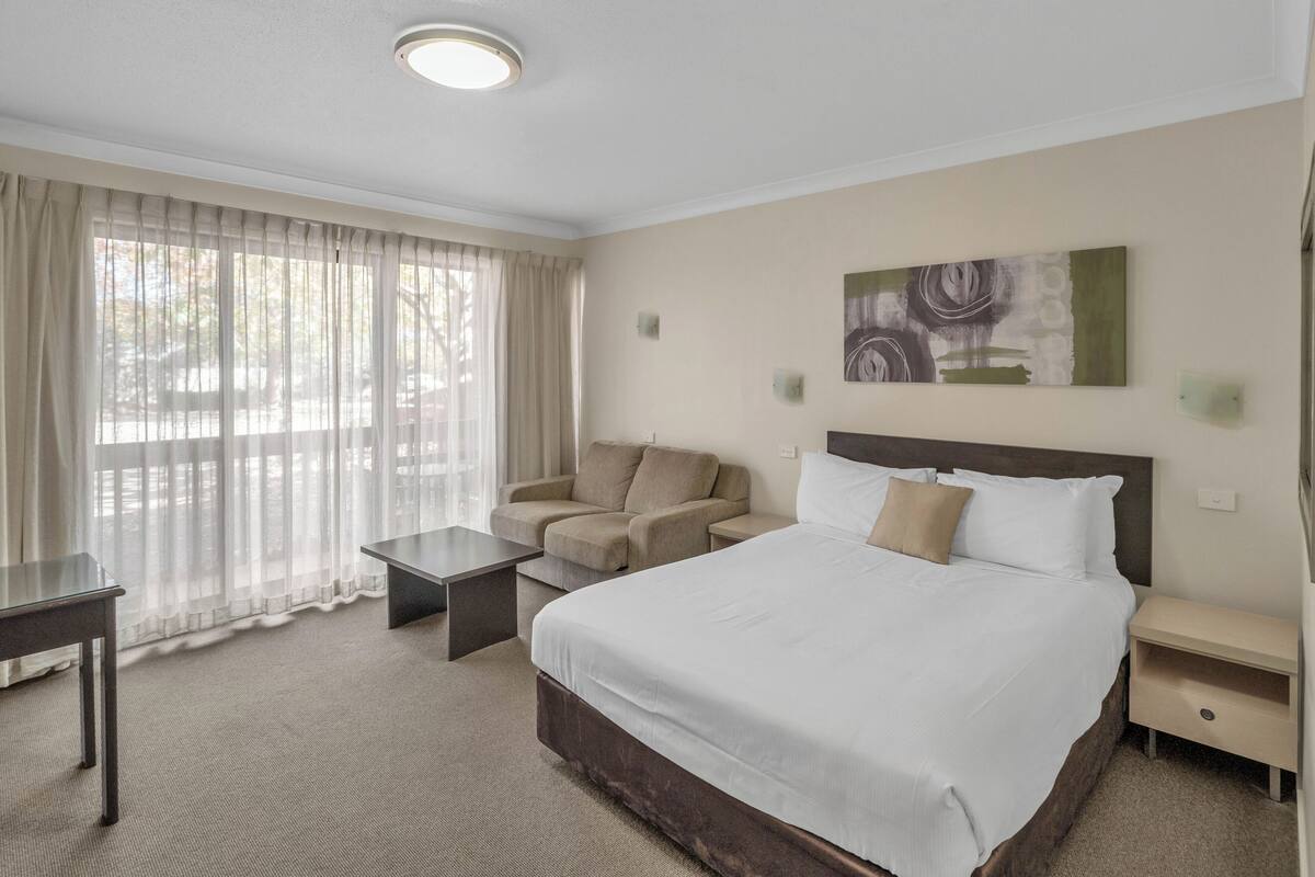 A hotel room with a bed, a sofa, a small table, and a window with curtains.