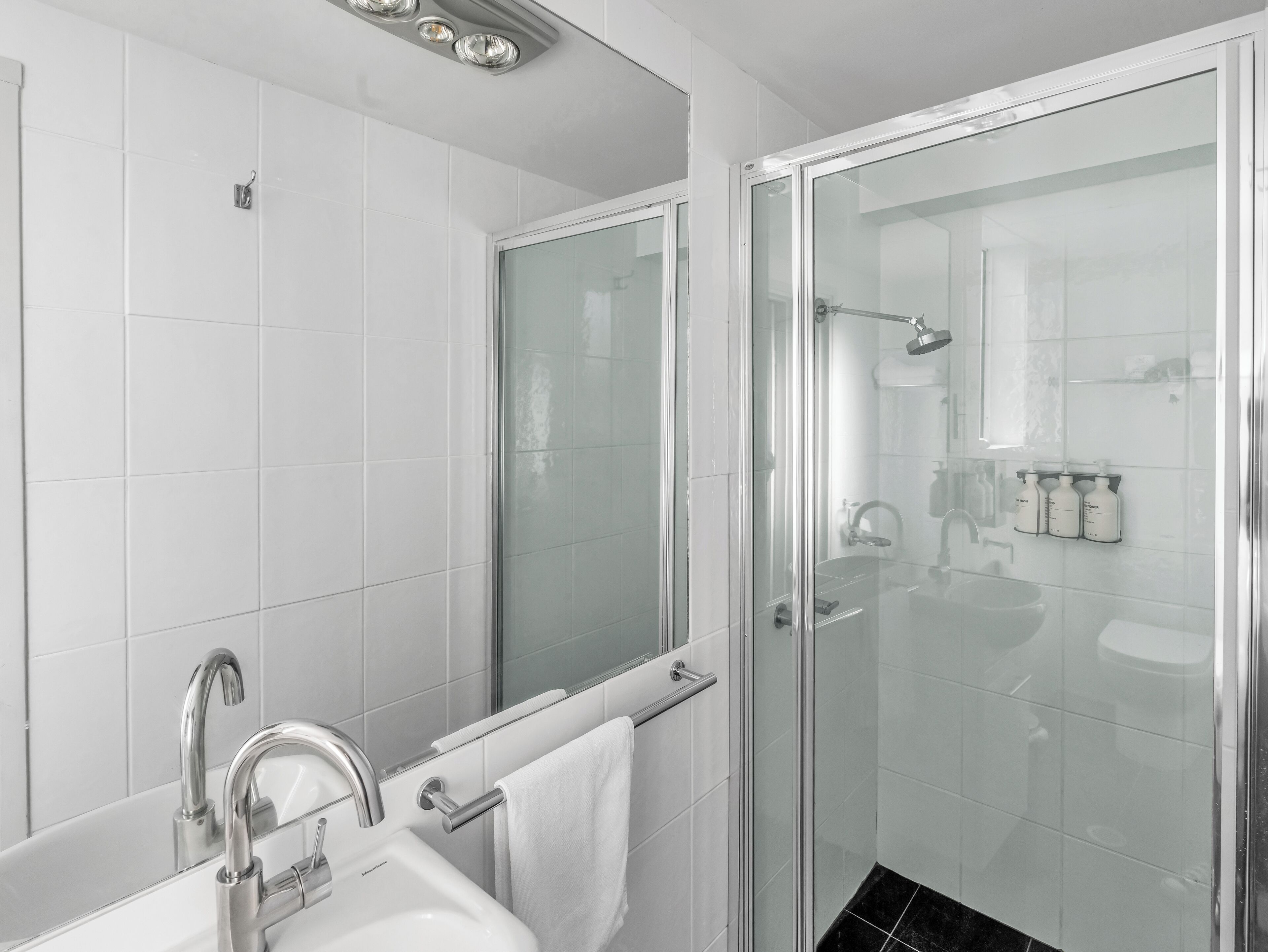 Ein modernes Badezimmer mit einer behindertenfreundlichen, gläsernen Dusche, einem weißen Waschbecken und einem Spiegel.