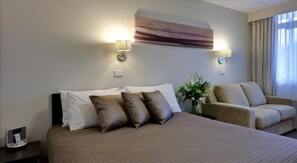A hotel room with a bed, a sofa, two wall-mounted lamps, a clock, and a window with curtains. - Tall Trees Ainslie Motel (Ainslie)