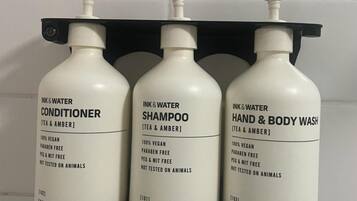 Tres botellas de productos INK&WATER sobre una pared de baldosas blancas.