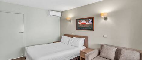 Una habitación de hotel con una cama, una mesita de noche, una lámpara, un sofá y un cuadro colgado en la pared.