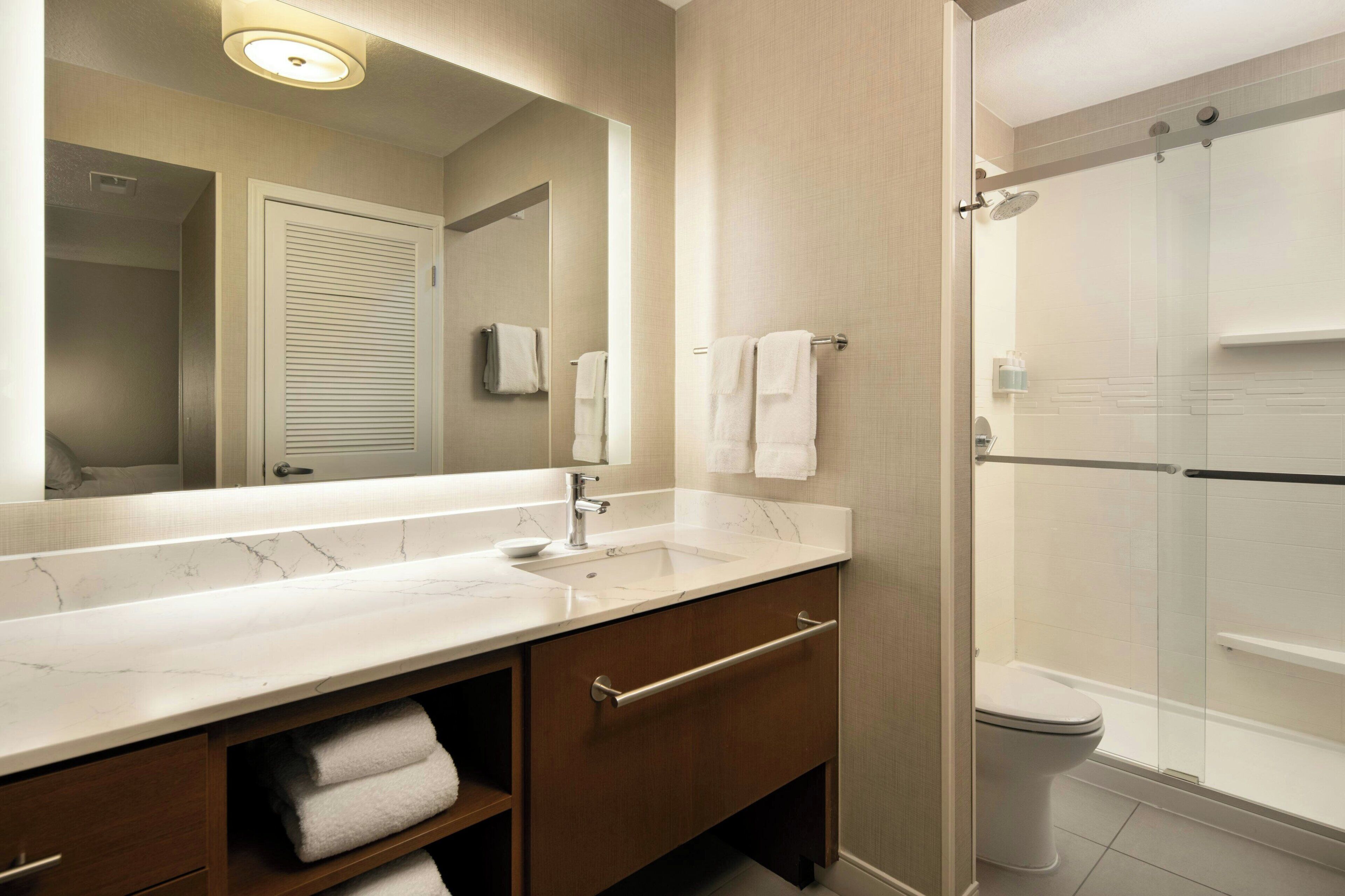 A bathroom with a marble sink, wooden vanity, a glass shower enclosure, and a toilet.