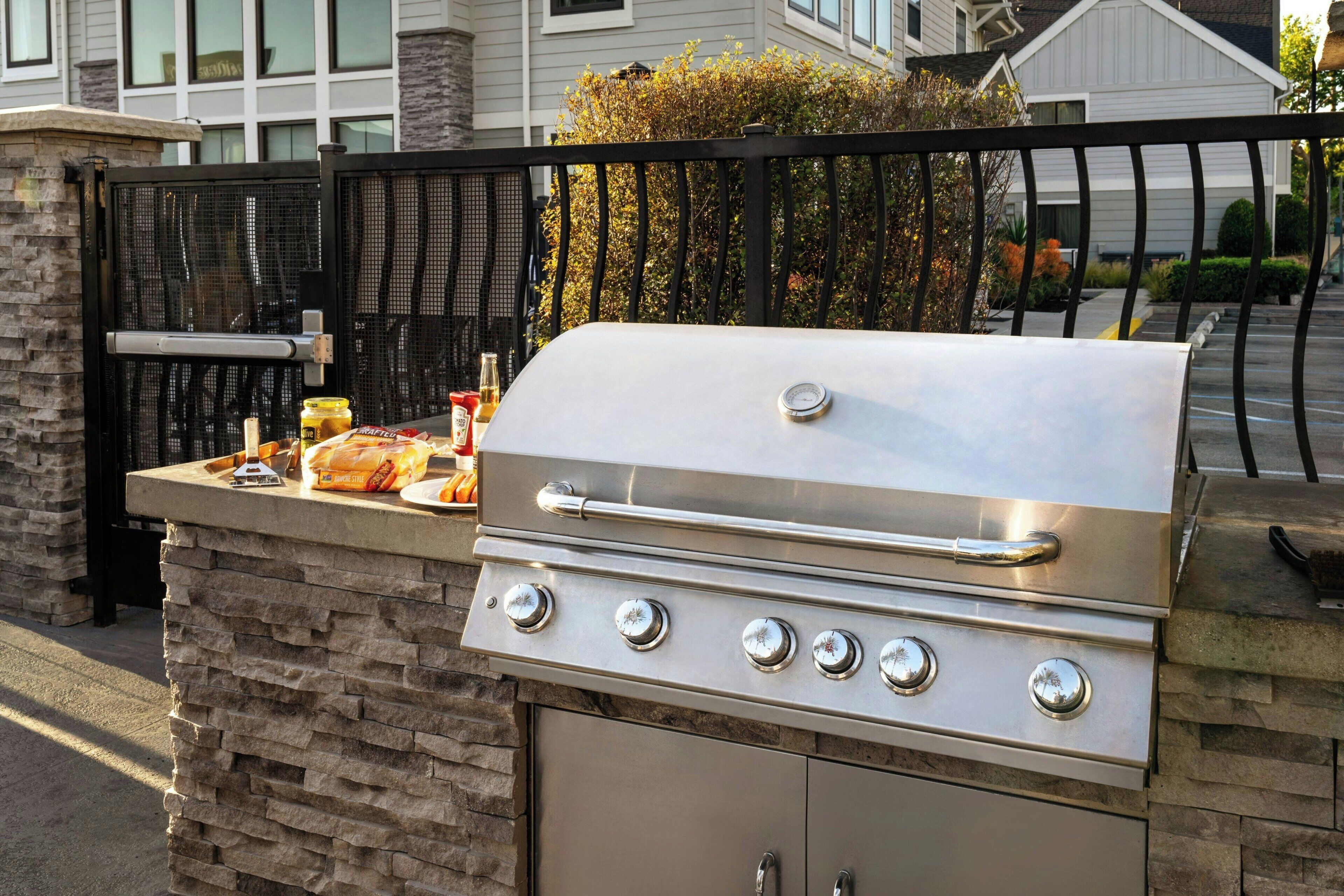 A stainless steel outdoor grill with four burners, a built-in storage cabinet, and a stone base.