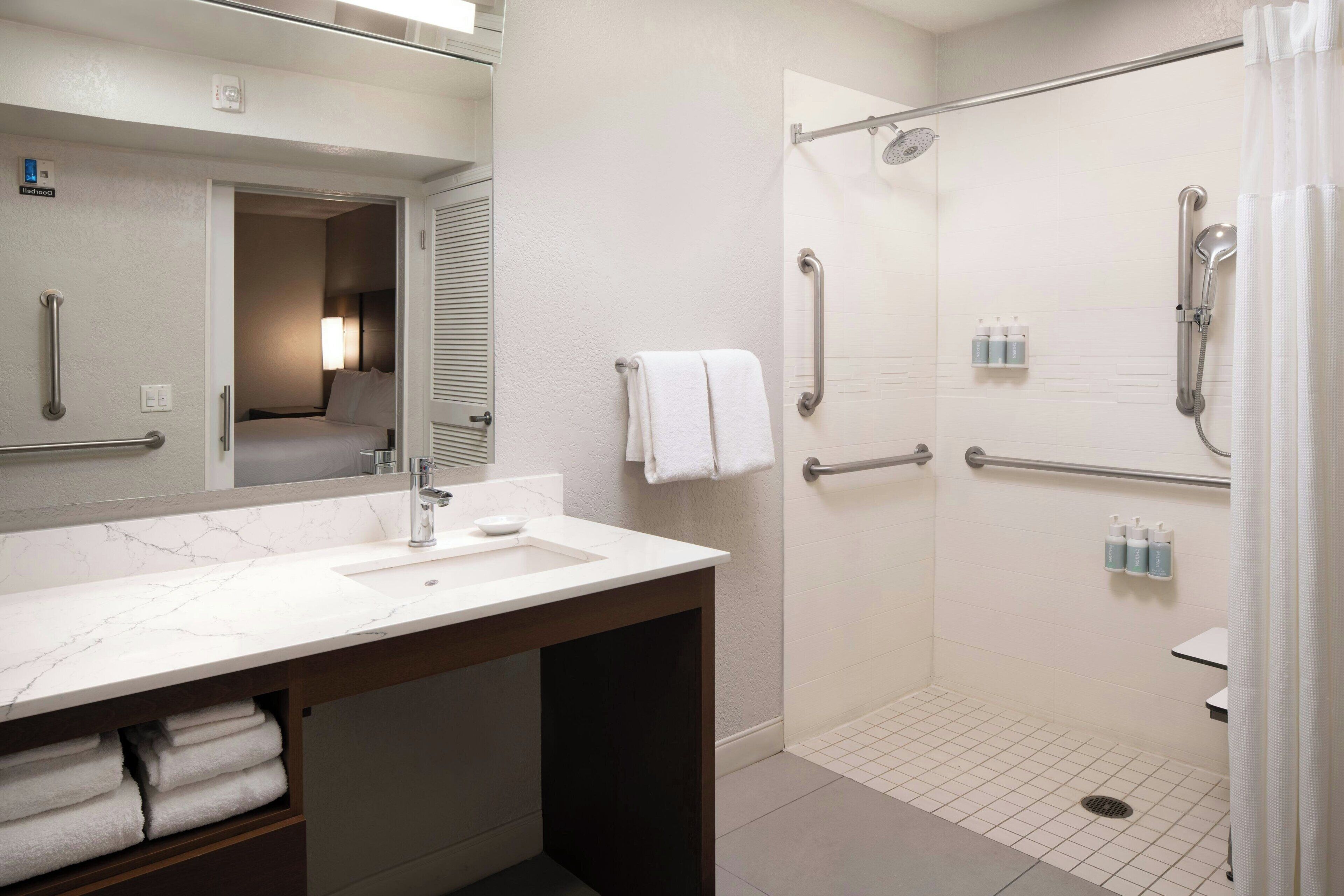 A bathroom with a marble sink, a shower with grab bars, and a towel rack.