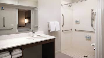 A bathroom with a marble sink, a shower with grab bars, and a towel rack.