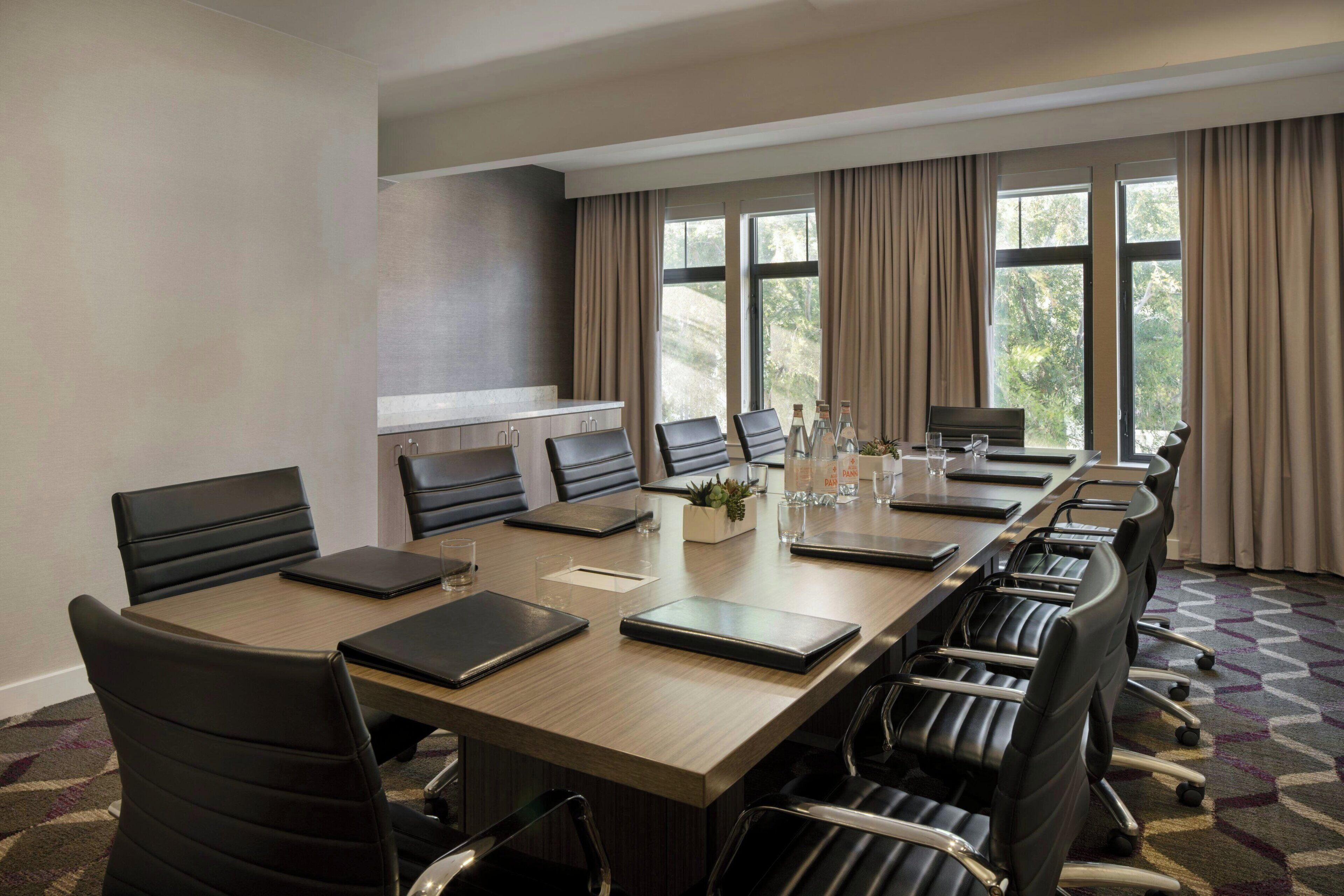 A conference room with a long table, multiple chairs, and a small kitchenette area.