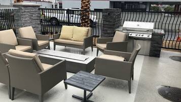 Ein Terrassenbereich im Freien mit Korbmöbeln, einem Grill und einer Steinpfeiler.