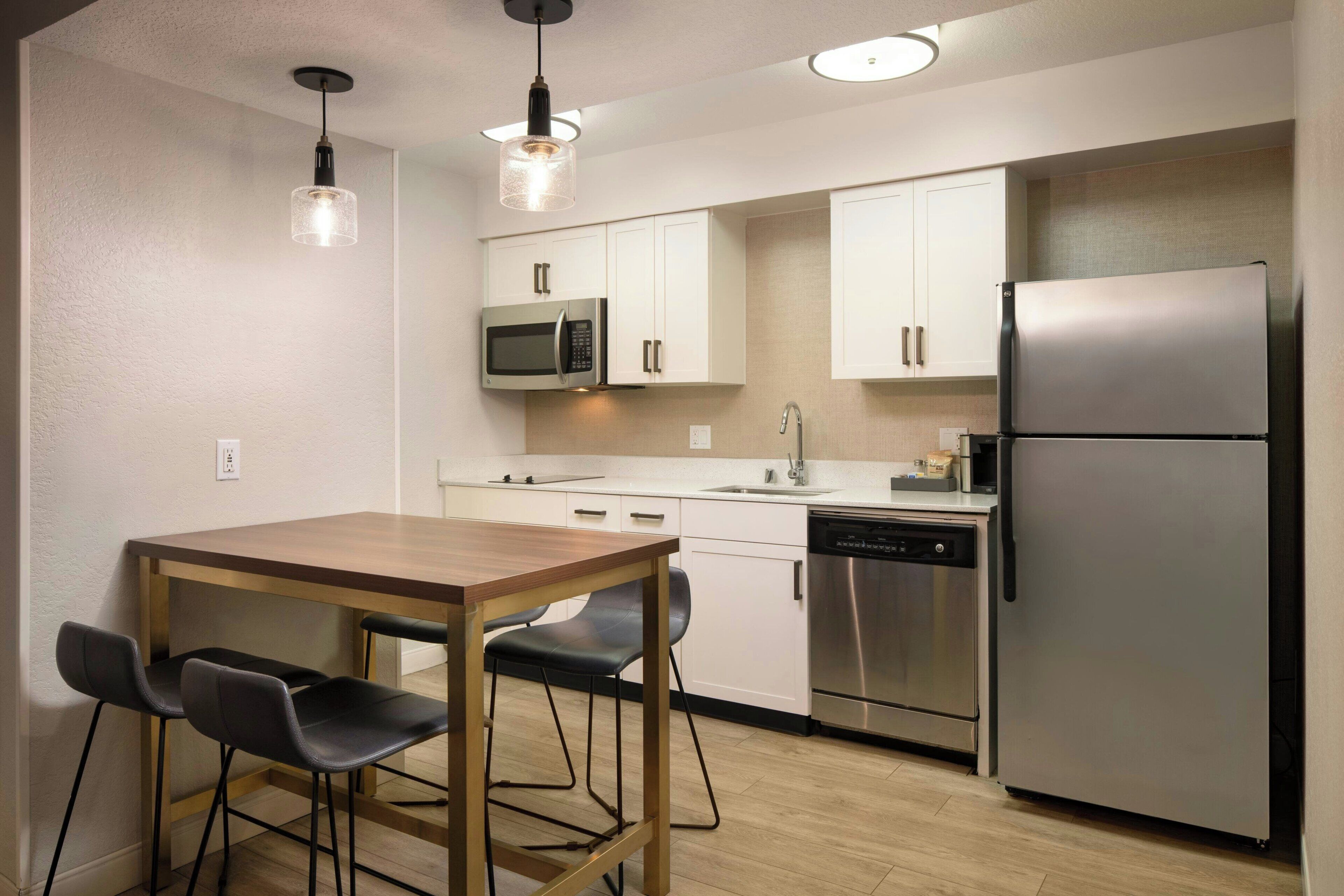 Una cocina moderna con una mesa de madera, dos sillas, un microondas, un lavavajillas y un refrigerador.
