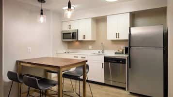 Una cocina moderna con una mesa de madera, dos sillas, un microondas, un lavavajillas y un refrigerador.