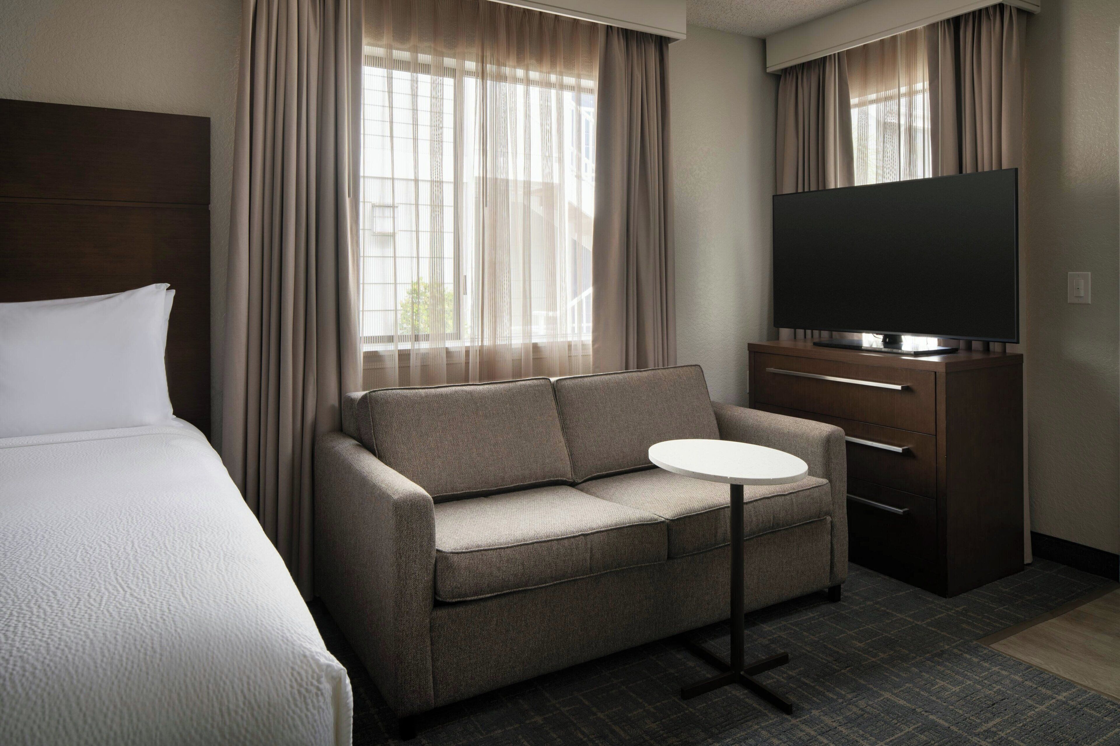 Une chambre d’hôtel avec un lit, un canapé, une télévision et une petite table.