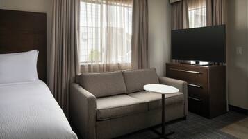 Une chambre d’hôtel avec un lit, un canapé, une télévision et une petite table.
