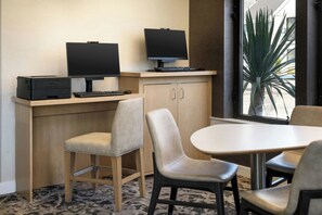 Habitación de hotel con escritorio, dos monitores, una impresora, un teclado y una silla.